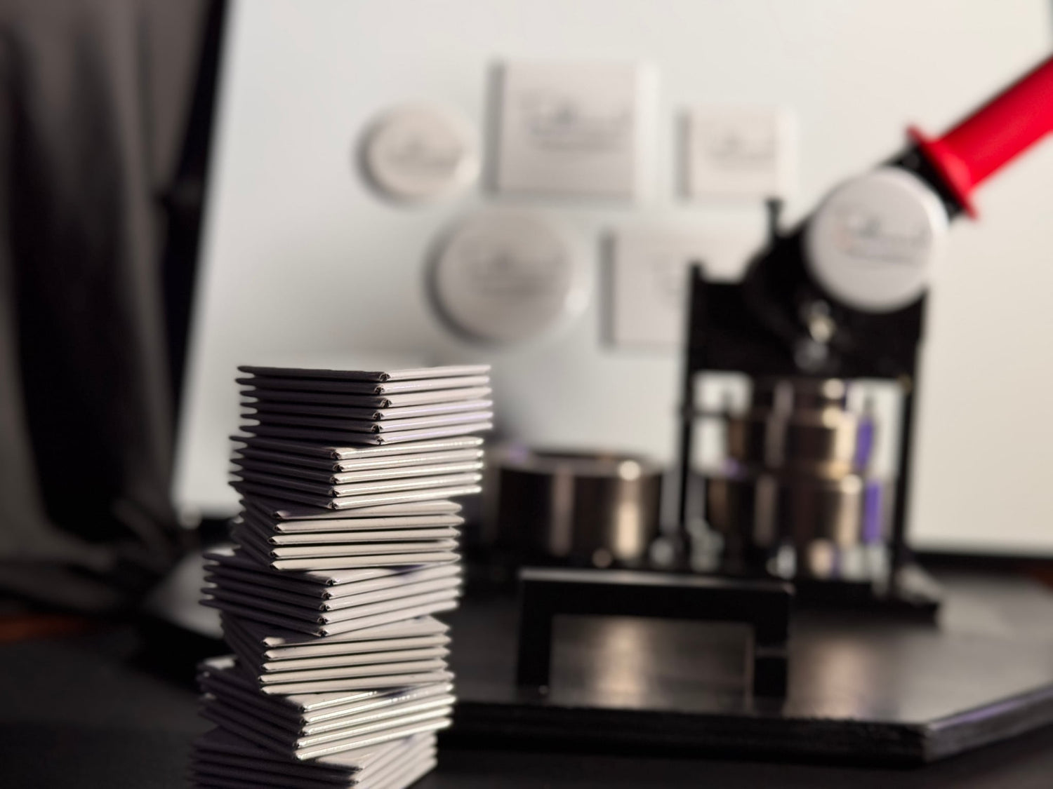 Image of custom square magnets stacked with a photo magnet making machine in the background