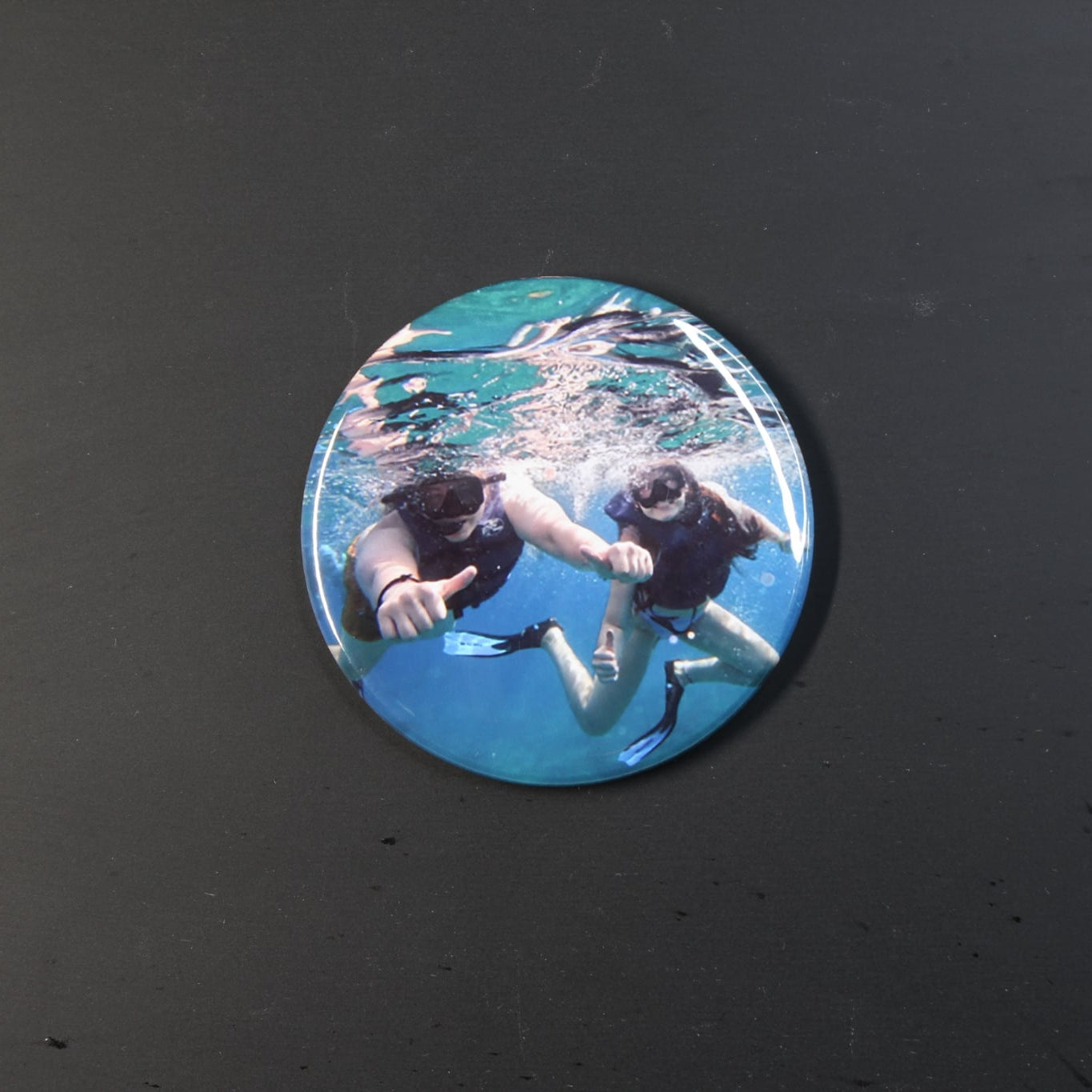 Circular photo magnet of two people underwater on a black background
